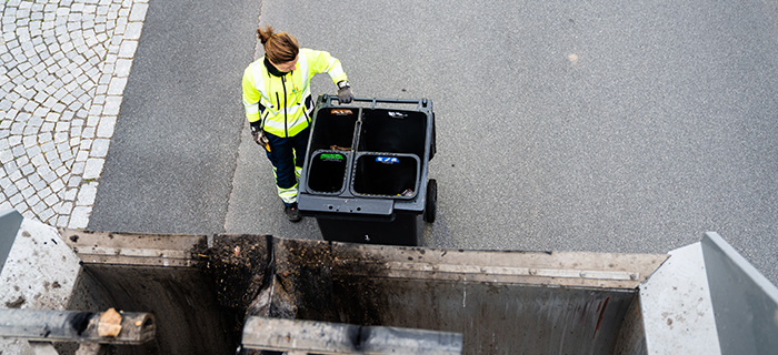 Bild tagen uppifrån en avfallsbil där en renhållningsarbetare står på marken och ska hissa upp kärlet för tömning. 